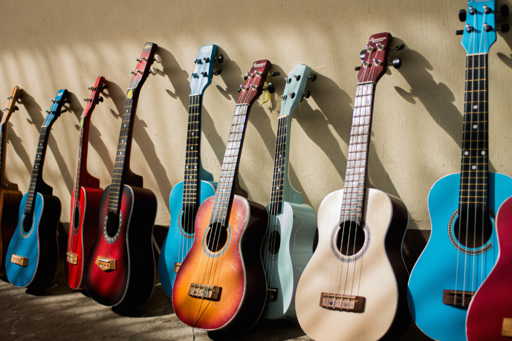 A selection of colorful guitars lined up along a wall. Sunlight shines on them.